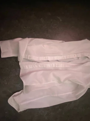 Vit klassisk skjorta med knappar - Stilren vit skjorta med lång ärm och knappar framtill. Skjortan har klassisk krage och är tillverkad i ett lätt bomullstyg som känns fräscht och passar till många olika looks. Perfekt basplagg för garderoben.