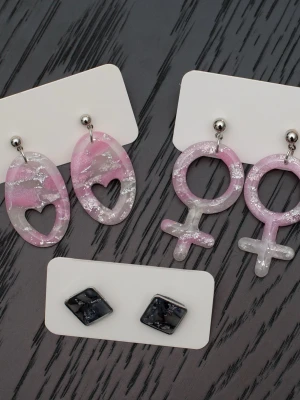 Handgjorda örhängen i polymerlera och stift i rostfritt stål feminist kvinnosymbol rosa - Handgjorda örhängen i polymerlera och stift i rostfritt stål.  Självklart nya och oanvända. Storlek: Ovala med hjärtan 2x4cm. Kvinnosymbol 2,5x5cm. Stiftörhängen 1,5x1,5cm.  Färgerna kan variera beroende på skärminställningar.