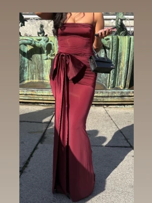 Vinröd balklänning med rosett - Snygg vinröd långklänning, som passar perfekt nu inför Bal säsongen. Klänningen är från oh polly och har endast använts en gång. Storlek 4(xxs, passar även xs) Köpt för ca 1100kr. Pris kan diskuteras 