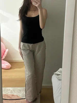 Beige linnebyxor med bred passform - Säljer ett par beige linnebyxor med bred passform och elastisk midja. Byxorna är tillverkade i ett lätt och luftigt linnematerial som är perfekt för varma dagar. De har en enkel design utan fickor och faller snyggt längs benen.