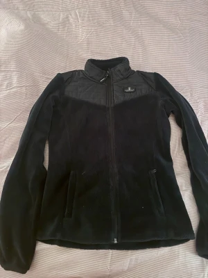 Blå fleecejacka från Kingsland - Mysig blå fleecejacka från Kingsland med hel dragkedja och hög krage. Jackan har quiltade detaljer över axlar och bröst, två fickor med dragkedja och broderad logga på bröstet samt stor logga på ryggen. Perfekt för kyliga dagar och snygg till vardagslooken.