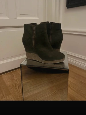 Mörkbruna kilklackade stövletter - Snygga mörkbruna stövletter i mockaimitation med kilklack och dragkedja på sidan. Skorna har en rundad tå och en stabil klack i korkliknande material. Perfekta för dig som vill ha både höjd och komfort i din stil.