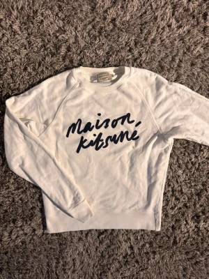 Vit sweatshirt Maison Kitsuné🙌🤩 - Säljer en vit sweatshirt från Maison Kitsuné med svart handskriven logga på bröstet. Tröjan har rund halsringning och långa ärmar. Tillverkad i mjukt bomullsmaterial som är skönt mot huden. Perfekt för en avslappnad och stilren look. Kom med prisförslag 🙌🤩
