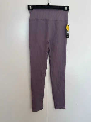 Lila ribbade träningsbyxor från NA-KD i strl S (36-38) - Säljer ett par lila ribbade leggings från NA-KD i storlek S (36/38). De har hög midja och är tillverkade i ett stretchigt material som sitter skönt på kroppen. Perfekta för en avslappnad och trendig look.Djur och rökfritt hem 