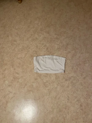 Vit bandeau tubtopp - En enkel och stilren vit bandeau tubtopp i mjukt material. Toppen är axelbandslös och har en rak passform som sitter tight runt överkroppen. Perfekt att matcha med höga jeans eller kjol för en clean look.