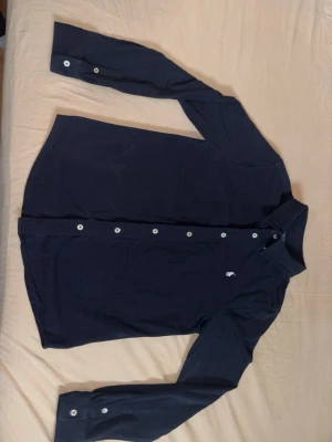 Mörkblå skjorta från Polo Ralph Lauren - Klassisk mörkblå skjorta från Polo Ralph Lauren med vita knappar och broderad logga på bröstet. Skjortan har lång ärm och är tillverkad i mjuk bomull. Perfekt för en stilren look. Nästan inte använd