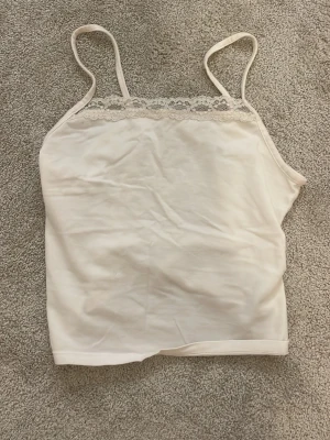 Vit spetsdetaljerad linnetopp H&M - Söt vit linnetopp från H&M med tunna axelband och spetsdetalj längs urringningen. Perfekt att styla till jeans eller kjol för en enkel och fräsch look. Tillverkad i mjuk bomull som känns skön mot huden. storlek 146/152❤️