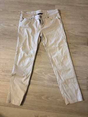 Beige chinos från Jacob cohen - Snygga beige chinos från Jacob cohen med klassisk rak passform och fem fickor. Byxorna har bälteshällor, knappgylf och detaljer som den lilla italienska flaggan på bakfickan.