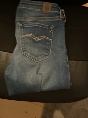 Blå slim fit jeans med bakficka - Snygga blå slim fit jeans med klassisk femficksdesign och cool detaljsöm på bakfickan. Jeansen har en läderpatch i midjan och är tillverkade i ett mjukt denimtyg som ger en skön passform. Perfekta för dig som gillar en enkel men trendig look.