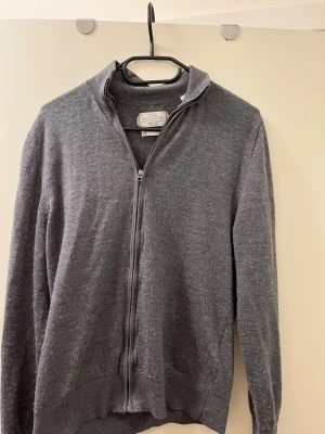 Grå ziptröja från These Glory Days - Säljer en stilren grå ziptröja från These Glory Days. Tröjan har hög krage, hel dragkedja och är tillverkad i mjukt material som passar perfekt för lager-på-lager. Skandinavisk design med ribbade muddar och klassisk look.