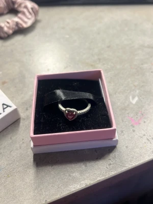 Pandora ring med rött hjärta - Söt silverfärgad ring från Pandora med ett rött hjärta i mitten. Ringen har en pärlad design runt hela bandet och kommer i original ask. Perfekt för dig som vill ha en romantisk och stilren accessoar.