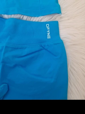 Blått underklädesset från DFYNE - Säljer ett blått underklädesset från DFYNE med en sömlös topp och matchande shorts. Setet har bred resår i midjan och logotypen är tryckt i vitt på både topp och shorts. Materialet är stretchigt och bekvämt, perfekt för en sportig look.