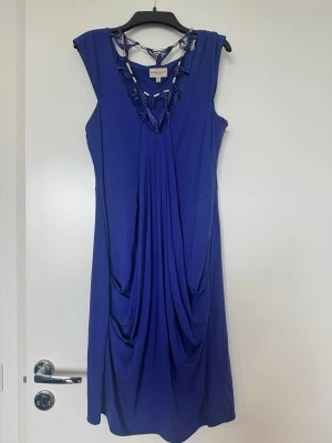 Blå klänning från Karen Millen - Säljer en fantastisk klänning från Karen Millen i en djup koboltblå färg strl 40  Klänningen har en unik design med vackra draperingar framtill som ger en smickrande silhuett. Den har även en dekorativ halsringning med flätade detaljer och metallinslag som gör den extra speciell. 	•	Märke: Karen Millen 	•	Färg: Blå / kobolt 	•	Storlek: UK 12, US 8, EU 40 	•	Modell: Knälång 	•	Ärmlös 	•	Dragkedja i sidan 	•	Fodrad och i stretchigt, följsamt material  Perfekt till fest, middag. I bra använt skick