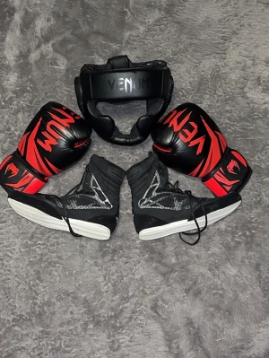 Komplett boxningskit från Venum – ”(ART 1)” -  ett kit med högkvalitativ kampsportsutrustning från Venum. Perfekt för både nybörjare och dig som tränat ett tag. Utrustningen är i mycket gott skick. * !!BONUS: Skickar även med ett hopprep, adidas tandskydd och boxningslindor helt gratis vid köp av hela paketet! * Venum Contender Boxningsskor:  Stl 43  * Venum Challenger 3.0 Handskar: 12oz  * Venum Challenger 2.0 Huvudskydd: One size. Hämtas på plats eller skickas. Skorna har använts  mer men fortfarande jätte bra Nypris ca3000kr hämta/skicka