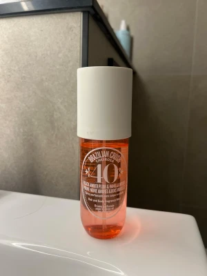 Brazilian Crush Cheirosa 40 mist - Fräsch och söt doftmist från Sol de Janeiro, Brazilian Crush Cheirosa 40. Flaskan är genomskinlig med orange ton och har en vit spraykork. Doften har inslag av svart bärnsten, plommon och vaniljträ. Perfekt att spraya i håret eller på kroppen.