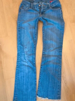 Blå bootcut jeans från seven - Ett par klassiska blå bootcut jeans från seven med slitna detaljer och fransad nederkant. Jeansen har fem fickor, knapp och dragkedja framtill samt tydliga sömmar. Perfekt för dig som gillar en avslappnad och trendig look.