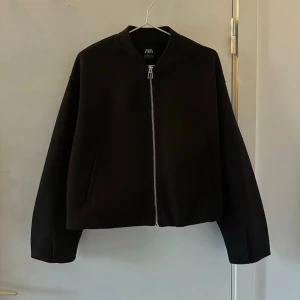 Svart bomberjacka från Zara - Stilren svart bomberjacka från Zara med klassisk rak passform och silverfärgad dragkedja framtill. Jackan har ribbade muddar vid hals, ärmslut och nederkant samt två snedställda fickor. Passar S och M. Använd endast en gång.💛