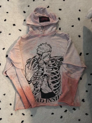Jujutsu Kaisen Hoodie - Cool hoodie i ljusrosa med svart Sukuna-tryck på framsidan. Hoodien har huva med knappar och långa ärmar. Perfekt för dig som gillar edgy streetstyle och anime. One of a kind, custom hoodie from Korea-based designer SKOOT.