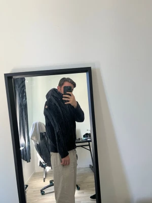 Svart hoodie från Moncler med huva - Säljer en svart hoodie från Moncler med stickad struktur och quiltad huva. Hoodien har dragkedja framtill och Moncler-logga på ärmen. Perfekt för dig som vill ha en snygg och exklusiv look. Materialet är en mix av stickat och vadderat tyg.