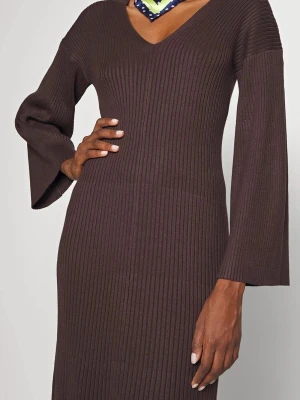Brun ribbad långklänning med v-ringning - Mörkbrun ribbad långklänning med v-ringning och vida långärmar. Klänningen har en figurnära passform och är tillverkad i ett stickat material som ger en mjuk och bekväm känsla. Perfekt för dig som gillar stilrena och tidlösa plagg.
