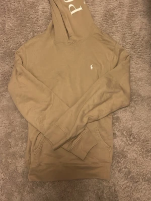 Beige hoodie från Polo Ralph Lauren - Snygg beige hoodie från Polo Ralph Lauren med klassisk huva och ficka framtill. Använd typ två gånger