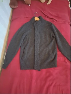 Mörkgrå stickad kofta från Barbour - Säljer en mörkgrå stickad kofta från Barbour med hög krage och dragkedja. Koftan har två fickor framtill och ribbstickade detaljer längs dragkedjan och i muddar. Perfekt för dig som gillar klassisk och stilren design.