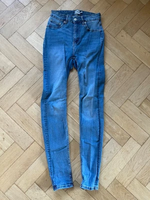 Blå skinny jeans med hög midja - Snygga blå skinny jeans med hög midja och klassiska fem fickor. Jeansen har en lätt tvättad look och smal passform som sitter tight hela vägen ner. Materialet är denim och de har dragkedja och knapp framtill. Från Lager 157 i modellen Snake.