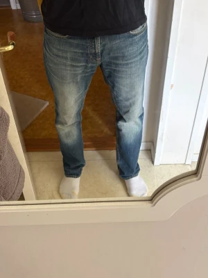 Straight fit jeans - Säljer ett par blå straight fit jeans med klassisk tvätt och ljusa slitningar på framsidan. Jeansen har fem fickor och normal midja. Perfekt för dig som gillar en avslappnad och tidlös look.