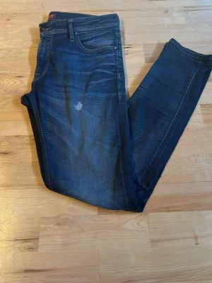 Mörkblå slim fit jeans - Snygga mörkblå slim fit jeans med klassisk femficksdesign och lätt slitna detaljer framtill. Jeansen har en smal passform och är tillverkade i ett stretchigt denimtyg för extra komfort. Perfekta för en trendig och avslappnad look.