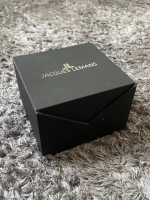 Jacques Lemans svart klockask - Snygg svart klockask från Jacques Lemans i stilren design. Asken är fyrkantig och har märkets logga i silver på locket. Perfekt för att förvara eller ge bort din klocka i en exklusiv förpackning. Helt Ny