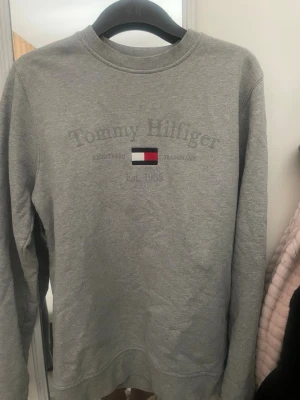 Grå sweatshirt från Tommy Hilfiger - Säljer en grå sweatshirt från Tommy Hilfiger med klassiskt broderat logotyptryck och flagga på bröstet. Tröjanä är i topp skick och används väldigt FÅ tal gånger !