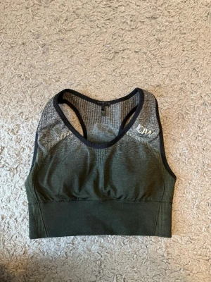 Grön sport-bh från ICANIWILL - Sport-bh i mörkgrönt och svart från ICANIWILL med brottarrygg och sömlös design. Tillverkad i stretchigt material och har vit logga på axeln. Bred ribbad resår under bysten för extra stöd.