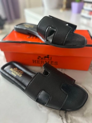 Svarta  lädersandaler - . Tillverkade i äkta läder och har en öppen tå samt platt sula. Perfekta för dig som vill ha en lyxig och tidlös look. Kommer med original orange box.