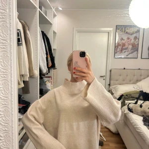 Oversize beige stickad tröja - Säljer en oversize stickad tröja i beige med hög krage och breda ribbade detaljer vid nederkant och ärmslut. Tröjan har långa ärmar och är gjord i mjukt material.