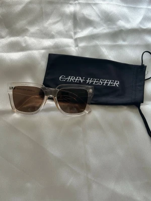 Transparenta solglasögon Carin Wester - Snygga solglasögon från Carin Wester med transparenta, fyrkantiga bågar och bruna glas. Perfekt accessoar för att höja din stil under soliga dagar. Medföljer svart fodral med logga. Bågarna är tillverkade i syntetmaterial. Kostar egentligen 200 kronor. 🥰
