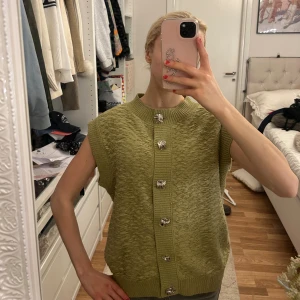Olivgrön stickad väst från Zara - Säljer en olivgrön stickad väst från Zara med korta ärmar och dekorativa silverfärgade knappar framtill. Köpt i London!!