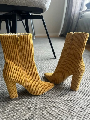 NLY Shoes  strl 38 Gula ribbade stövletter med klack - Snygga stövletter i gul ribbad textil med höga blockklackar och spetsig tå. Dragkedja på sidan för enkel påtagning. Perfekt för dig som vill sticka ut med ett trendigt statement.