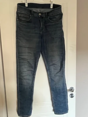 Blå slim fit jeans från Cheap Monday - Säljer ett par blå slim fit jeans med klassisk femficksdesign och snygga slitningar från legendariska Cheap Monday! Jeansen har bruna sömmar och är tillverkade i denim med stretch för extra komfort. Perfekt för dig som gillar en modern och stilren look. Strl 32/32. 