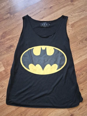 Fancycube Batman svart linne, storlek S eller ungdom - Tufft Svart linne med ett stort gult Batman-emblem tryckt framtill. Linnet har en rundad halsringning och ärmlösa axelband. Passar bra för en avslappnad stil. Storlek Small passar även ungdom 170 cl Märke: Fancyqube Mycket fint skick Djur och rökfritt hem