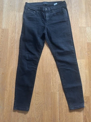 Svarta skinny jeans från Jack & Jones - Säljer ett par svarta skinny jeans från Jack & Jones med klassisk femficksdesign och knappgylf. Jeansen är tillverkade i stretchigt denim som ger en bekväm passform och snygg siluett. Perfekta för dig som gillar en slim look.
