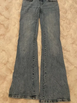 Blåa bootcut jeans med låg midja - Säljer ett par ljusblå bootcut jeans med låg midja och klassisk femficksdesign. Jeansen har en avslappnad passform med utsvängda ben och är tillverkade i denim. Perfekta för en trendig och avslappnad stil. Storlek XS Pris 40kr