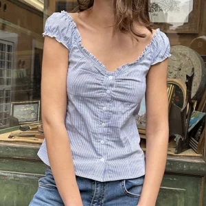 Blårandig blus med knappar - Söt blårandig blus med korta puffärmar och v-ringning. Blusen har knappar framtill och lätt rynkade detaljer vid axlar och byst. Perfekt till jeans för en avslappnad men ändå chic look. Aldrig använd, bara provat på! Den är liten i storleken.