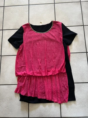 Svart och rosa topp med plisserad nederdel storlek XL - Unik topp med svart bas och en lös, rosa plisserad overlay. Rund halsringning med dekorativ kant och korta ärmar. Toppen har en avslappnad passform och ett lager-på-lager-utseende som ger en cool och modern vibe.