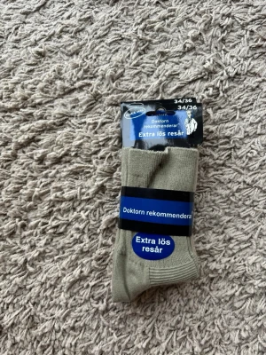 Beige strumpor från Sockcompaniet (helt nya) - Säljer tre par beiga/gröna/ljusrosa strumpor från Sockcompaniet med extra lös resår för skönare passform. Strumporna är tillverkade i 70% bomull, 25% polyester och 5% spandex. Perfekta för dig som vill ha bekväma och stilrena strumpor.