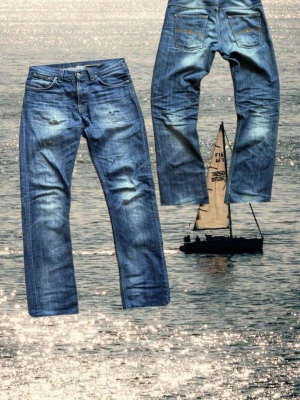 Vintage  jeans från Nudie  - Säljer ett par blå jeans från Nudie Jeans med snyggt slitna detaljer och tvättade partier. Klassisk femficksmodell med raka ben och kontrastsömmar. Jeansen har Nudie-logga på bakfickorna och är gjorda i mjuk bomullsdenim. Jeansen är i modellen Even Steven! 
