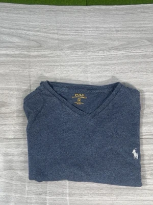 Blå V-ringad tröja Polo Ralph Lauren - Mörkblå V-ringad tröja från Polo Ralph Lauren med klassisk broderad logga i vitt på bröstet. Tröjan har en enkel och stilren design, perfekt för en avslappnad men snygg look. Materialet känns mjukt och bekvämt mot huden.