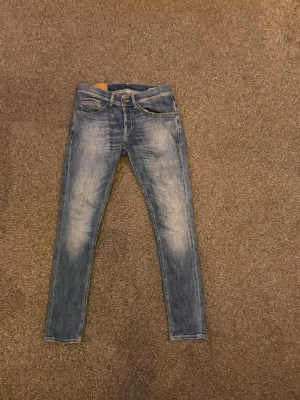 Blå slim fit jeans från Dondup - Säljer ett par blå slim fit jeans från Dondup med klassisk femficksmodell och snygga slitningar framtill. Jeansen har normal midja, smala ben och är tillverkade i denim med en tvättad look. Perfekta för en avslappnad och trendig stil.