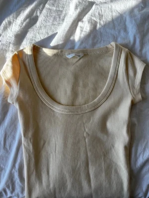 Beige ribbad topp med rund hals - Snygg beige ribbad topp med korta ärmar och djup rundad halsringning. Tillverkad i mjukt, stretchigt material som sitter skönt på kroppen. Aldrig använd 💓