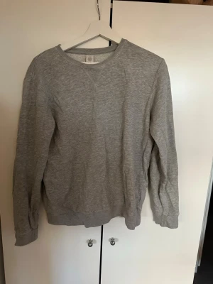 Grå basic sweatshirt  - En enkel och stilren grå sweatshirt med rund halsringning och långa ärmar. Tröjan har ribbade muddar vid ärmslut och nederkant. Perfekt för en avslappnad look och lätt att matcha med andra plagg. Storlek eur 170 dvs ca XS/S, skulle säga att det är storlek S.