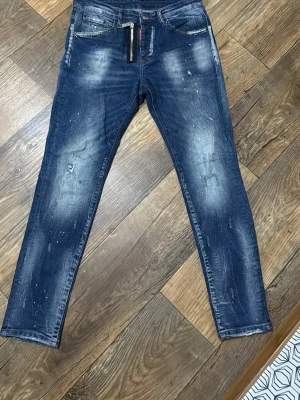 DSQUARED2 175-178 - Snygga mörkblå slim fit jeans med slitningar och ljusa partier på låren och knäna. Jeansen har klassisk femficksdesign och detaljer med färgstänk för en trendig look. Perfekta för dig som gillar en streetinspirerad stil.